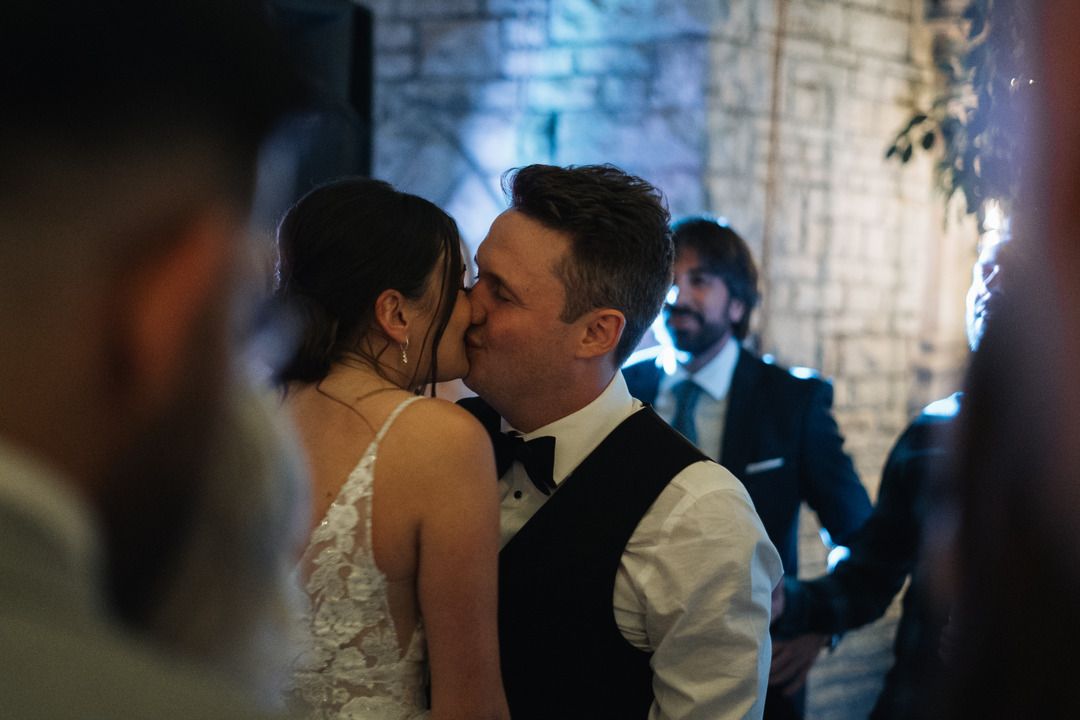 A photo of the bride and groom kissing after their first dance with the crowd out of focus between the photographer and the couple.
