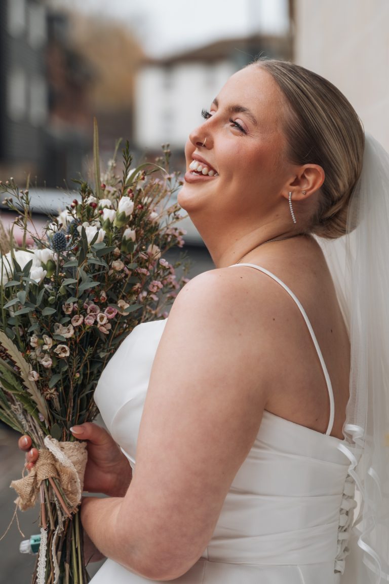 Bride leaning up against a wall and laughing whilst holding a boquet