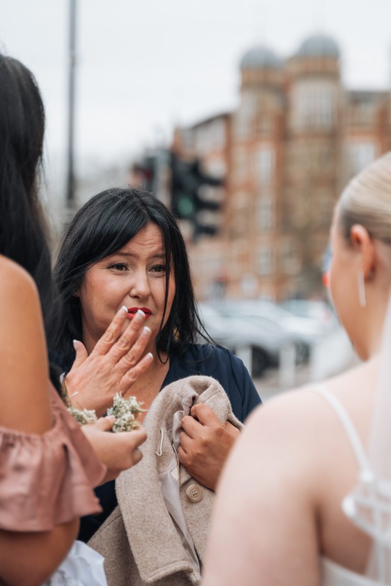 Mother of the bride seeing her daughter for the first time outside of Oxford Registry Office. She has her hand at her mouth in shock.