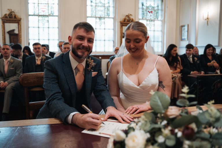 Groom smiling at the camera as he signs the register
