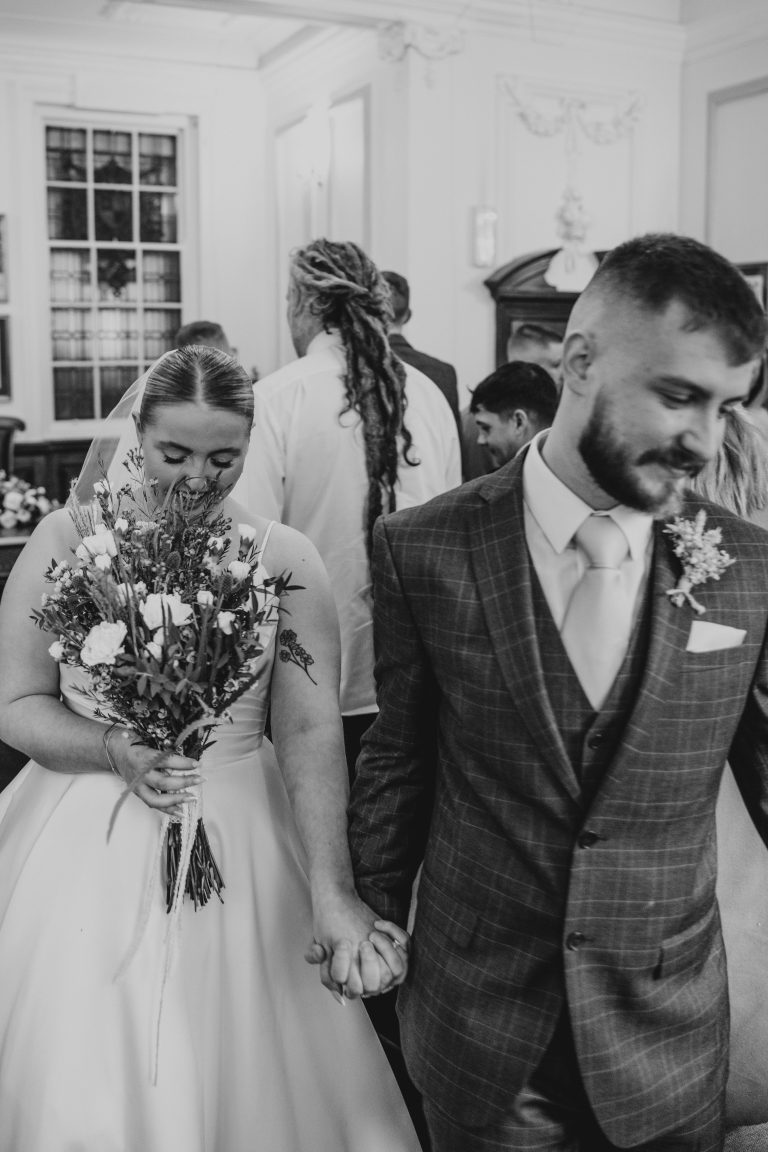 Bride and groom walking out of the ceremony room with the guests standing behind them