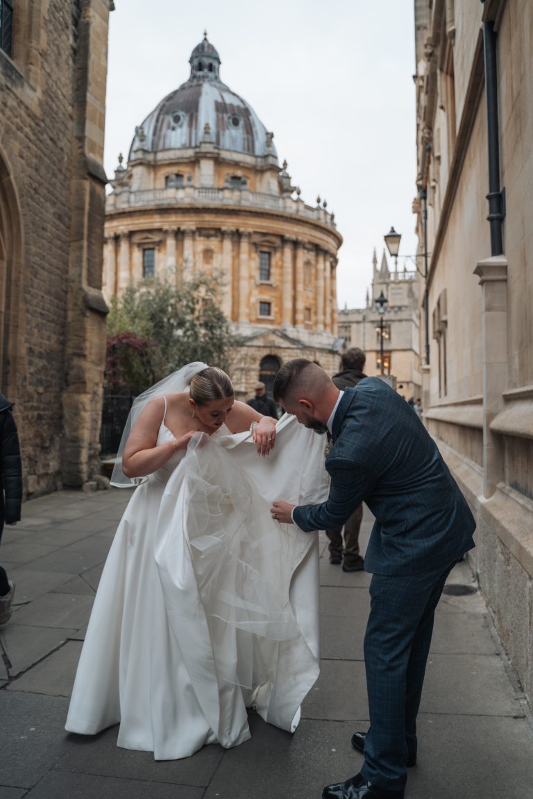 Groom sorting out the bride's outfit in front of the Radcliffe Camera in Oxford City centre.